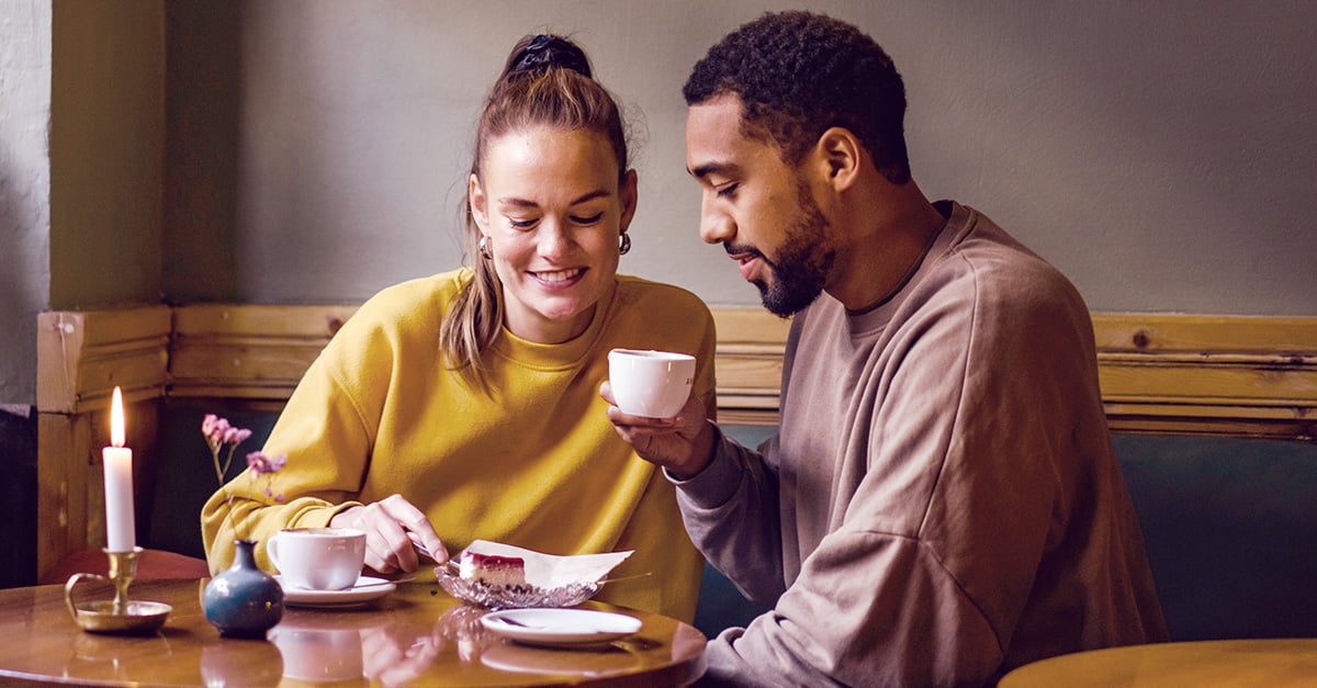 Zwei Singles beim Dating im Café, beide lächeln schüchtern, möchten aber die Absichten ihres Gegenübers wissen